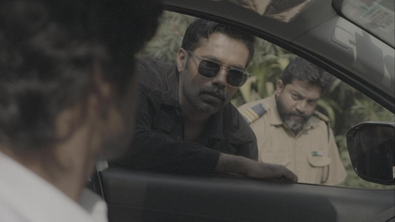F.I.R. Diaries: a man leans into a car window, policeman behind